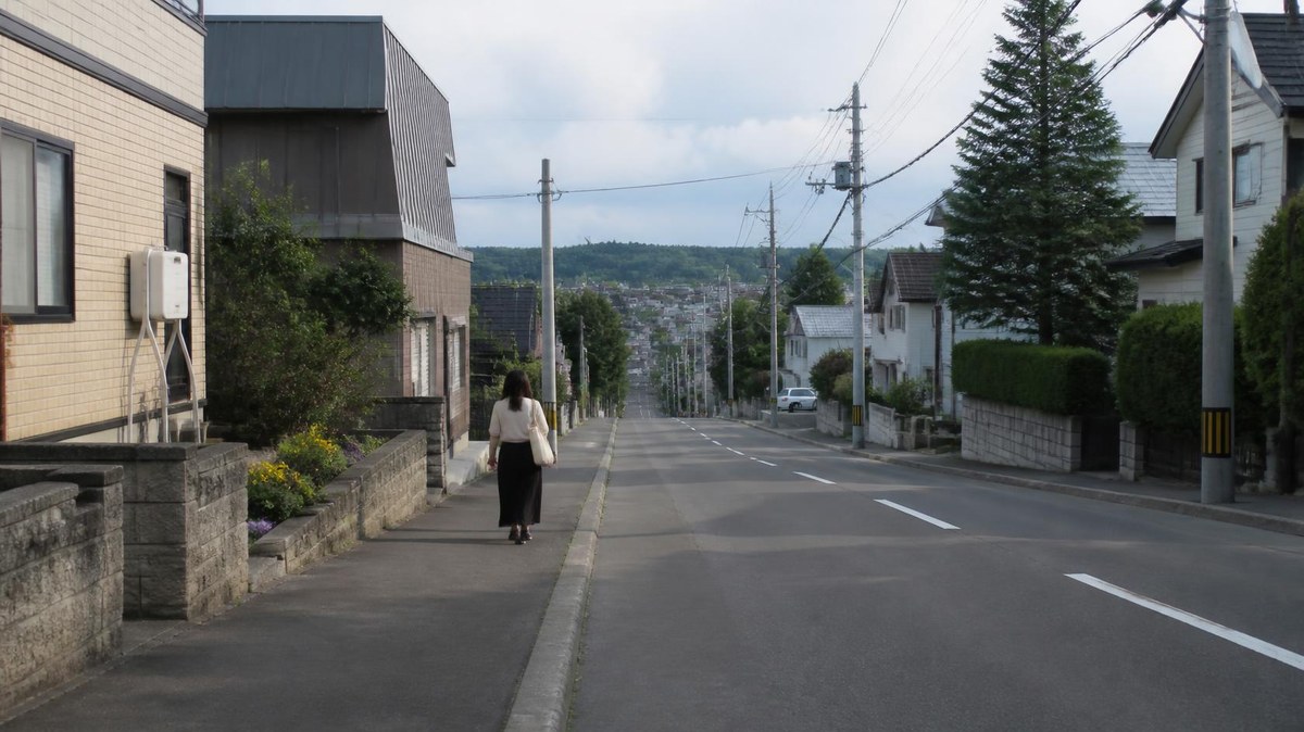 昼間の住宅街を歩く女性の後ろ姿(イメージ)