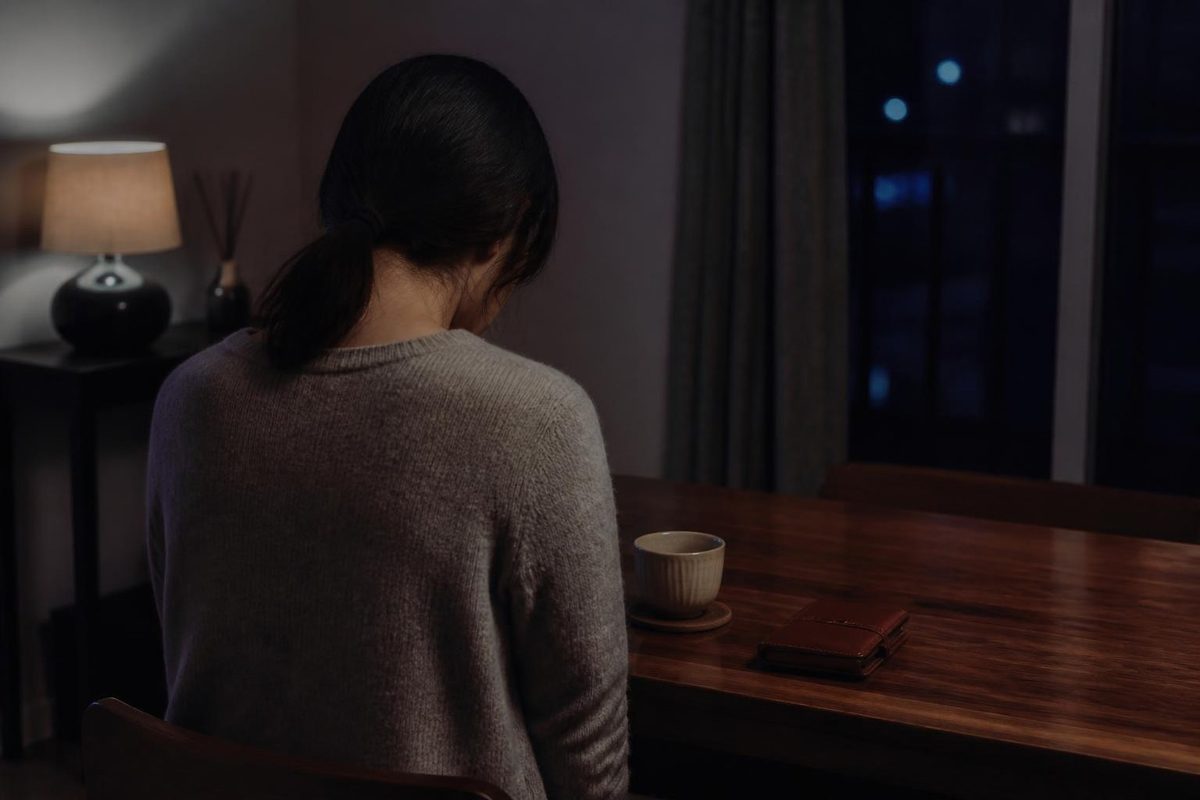 夜の食卓でうつむく女性の後ろ姿