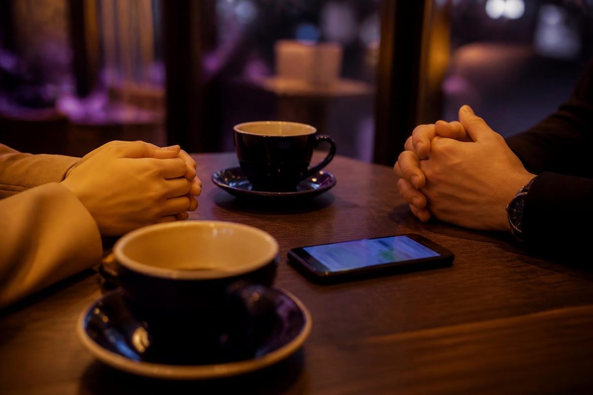 カフェのテーブルで向かい合う男女の手元とスマートフォン